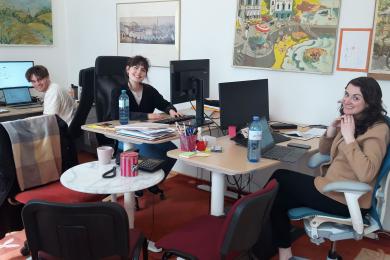 three staff members sitting at desks with computers smiling